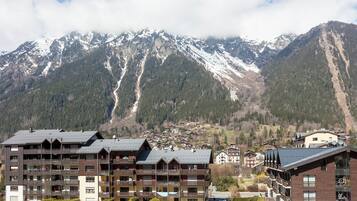 A multi-story hotel with balconies, set against a backdrop of snow-capped mountains and a clear sky.