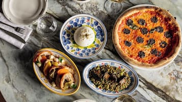 A round marble table with various dishes, including a pizza, a bowl of soup, and a plate of meat.