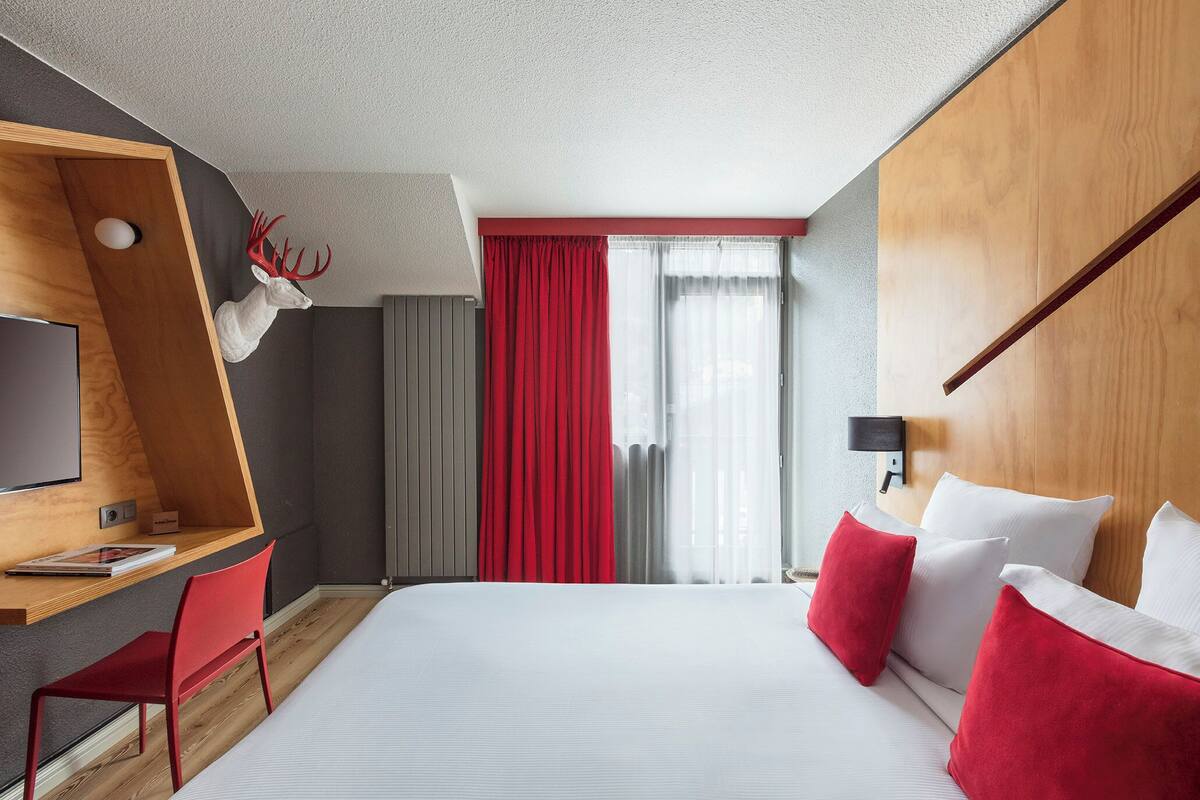 Een moderne hotelkamer met een groot bed, een bureau met stoel, een televisie en een decoratie van een hertenkop.