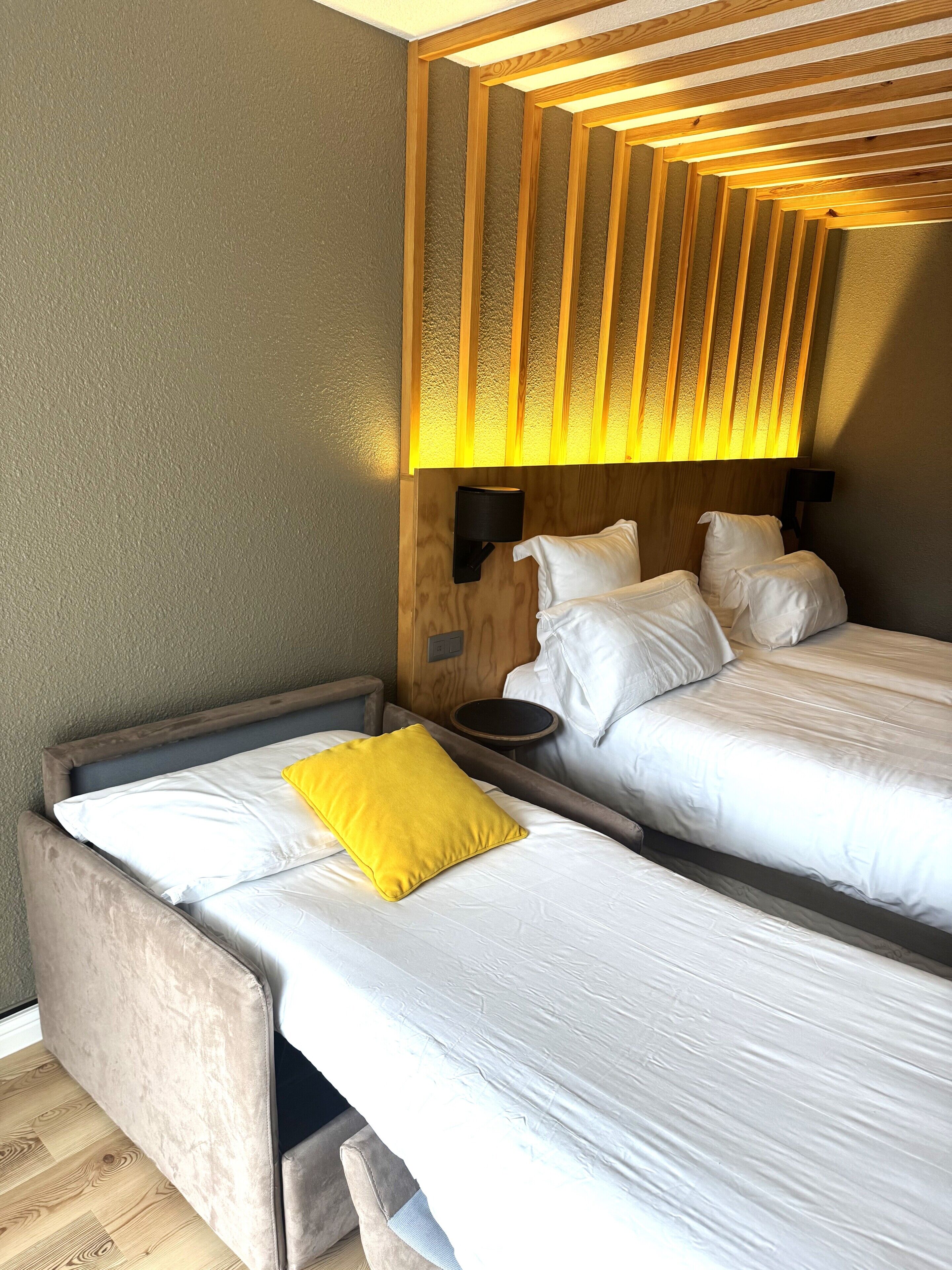 A double bed with white bedding and a yellow pillow, a bedside table, and a wooden headboard with vertical slats.
