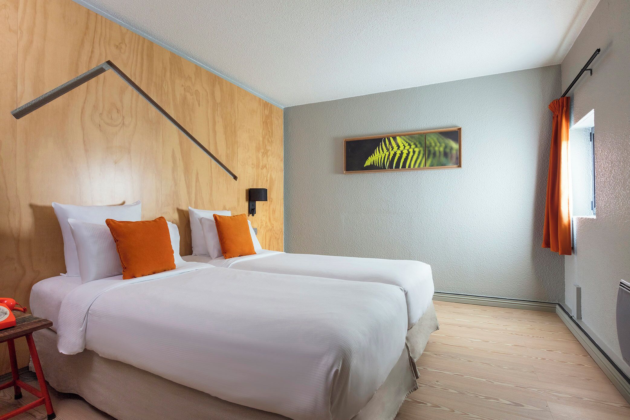 Ein Hotelzimmer mit zwei Betten, einer Holzwand, einem gerahmten Kunstwerk und einem Fenster mit Vorhängen.