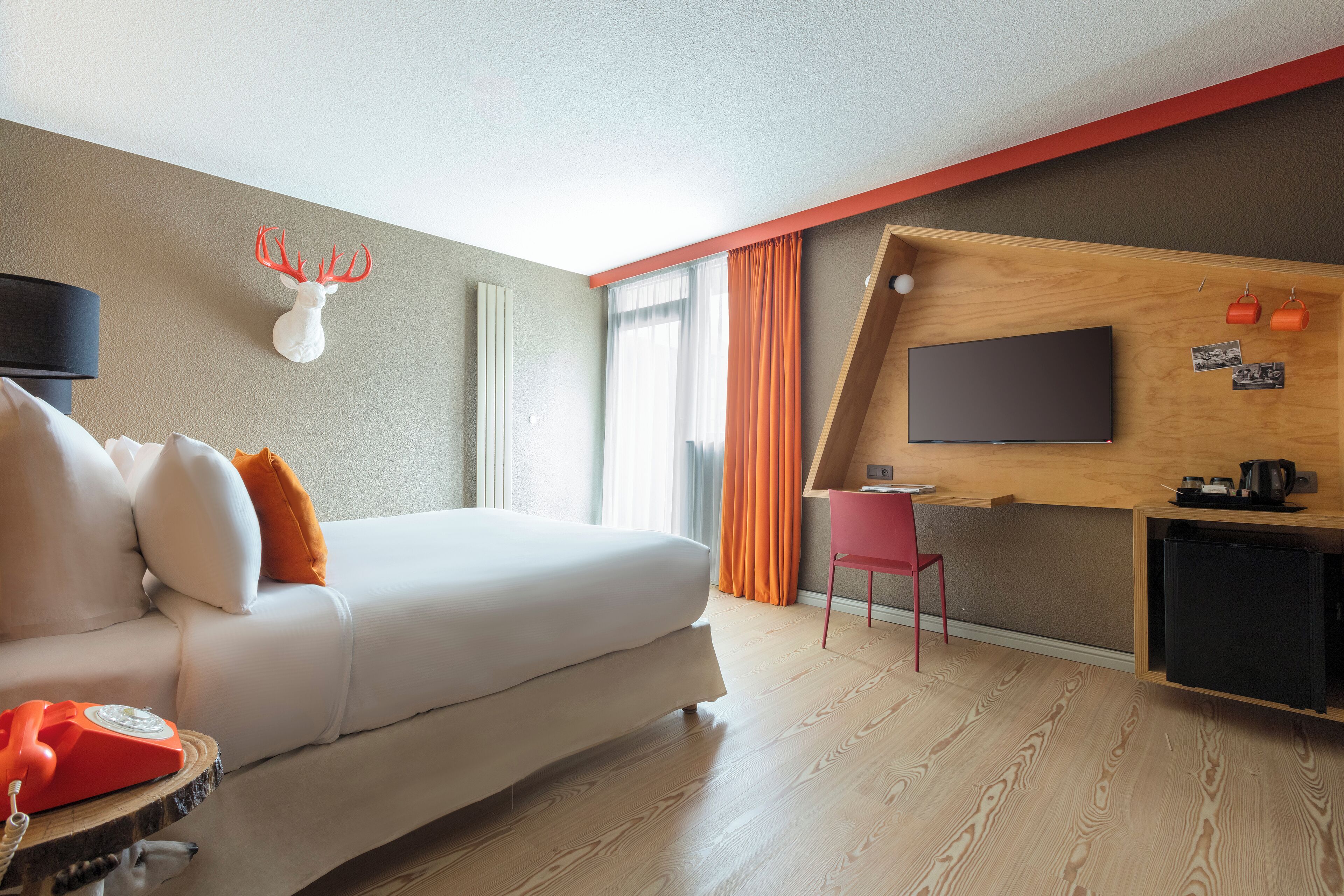 Ein modernes Hotelzimmer mit Bett, Schreibtisch, Fernseher und Holzboden.