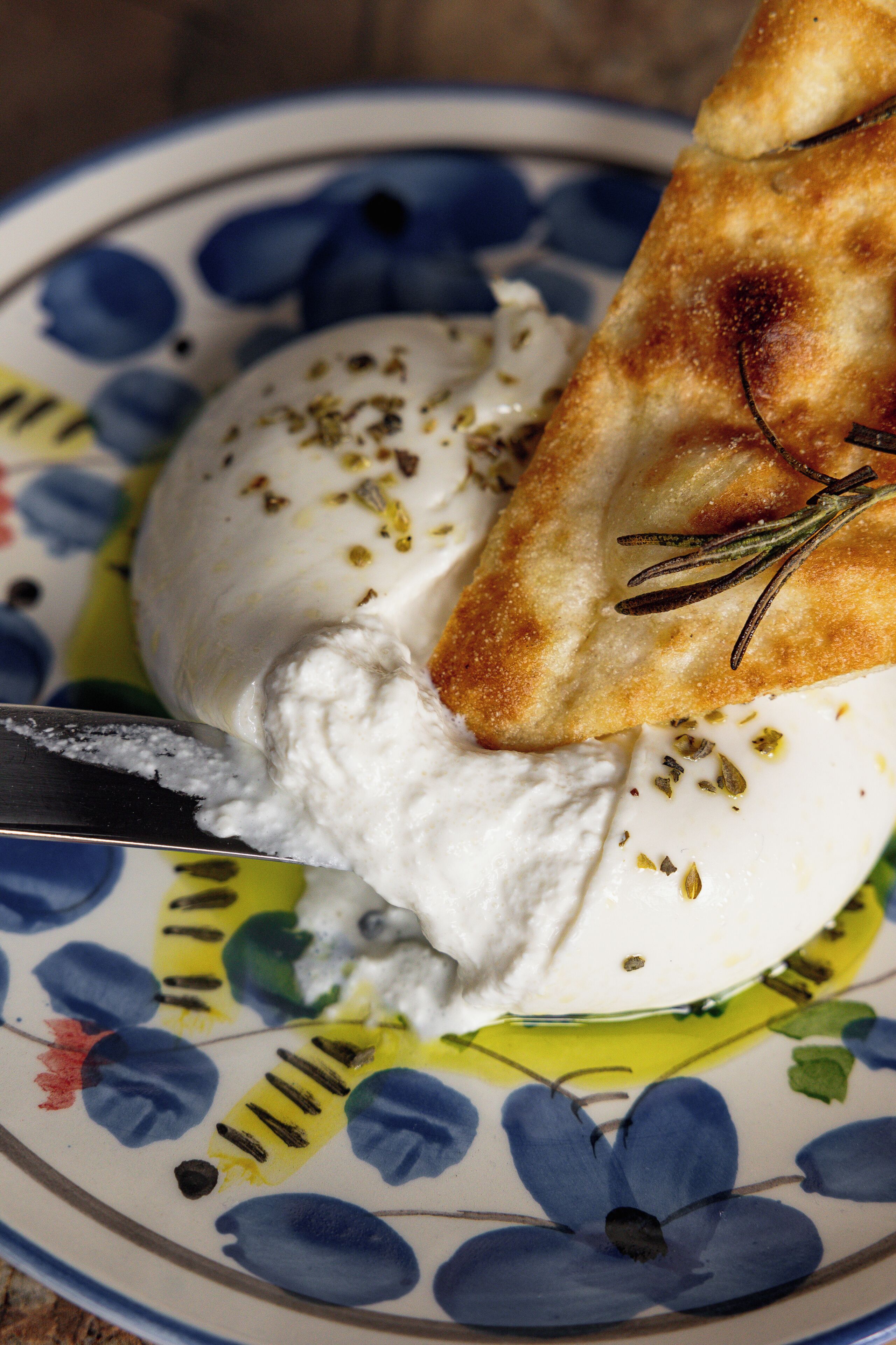 A plate with a white creamy substance, possibly cheese, garnished with herbs, and a piece of bread.