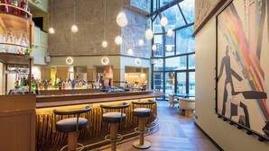 A bar area with a high ceiling, hanging lights, and a large window providing a view of the outside.