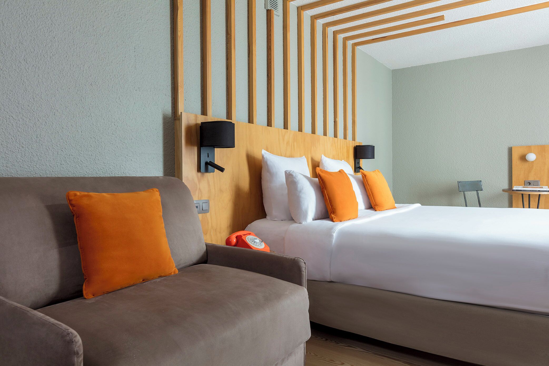 A hotel room with a bed, a sofa, and a wall-mounted lamp.