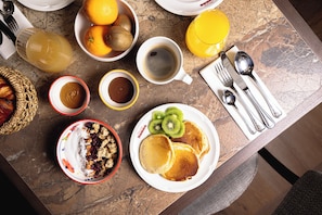 Une table de petit-déjeuner avec des crêpes, des fruits et des boissons.