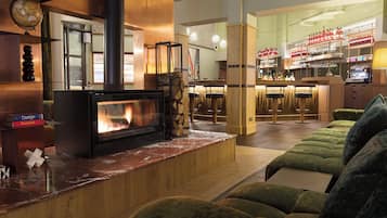 Un espacio de sala acogedor con chimenea, asientos tapizados en tono verde y una zona de bar con estantes llenos de botellas y vasos.