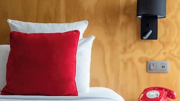 A bed with white and red pillows, a red rotary phone, and a black wall-mounted lamp.