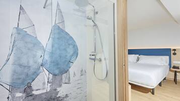 Una habitación de hotel moderna con cabina de ducha de vidrio, cama con ropa blanca y pared de acento azul.