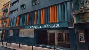Un edificio moderno con un cartel que dice "Occidental Alicante". Cuenta con múltiples ventanas de marcos naranjas y una fachada oscura.