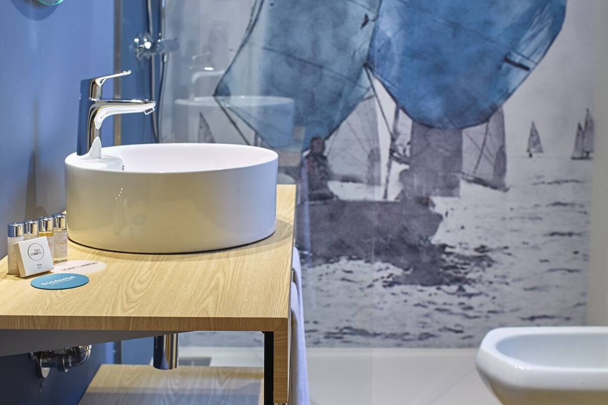 Une salle de bain avec un grand lavabo, un miroir et une douche. On y trouve un porte-serviettes avec des serviettes et une petite table avec des articles de toilette.