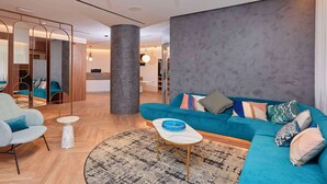 Un moderno vestíbulo de hotel con un sofá color esmeralda, un sillón azul claro y una mesa de centro redonda.