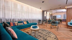 Una sala de estar moderna con un sofá color turquesa, una mesita redonda pequeña y un tapete estampado. Se observa un comedor con sillas y una mesa al fondo.