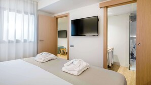 Ett hotellrum med en säng, en tv som är monterad på väggen och ett badrum som syns genom en öppen dörr.
