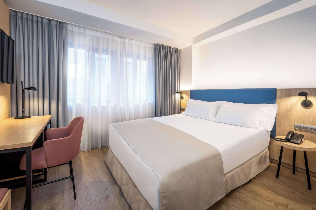 Une chambre d’hôtel équipée d’un lit, d’un bureau, d’une chaise, d’une télévision et d’une table de chevet avec un téléphone.