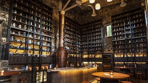 Un espace bar avec des tabourets de bar en bois, un comptoir central et des étagères remplies de bouteilles.