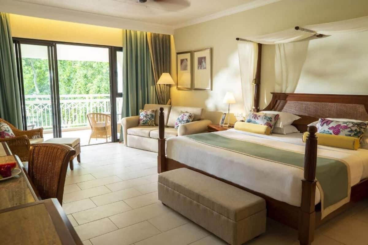 Ein Hotelzimmer mit Balkon, einem Himmelbett, einer Sitzecke und einem Esstisch.