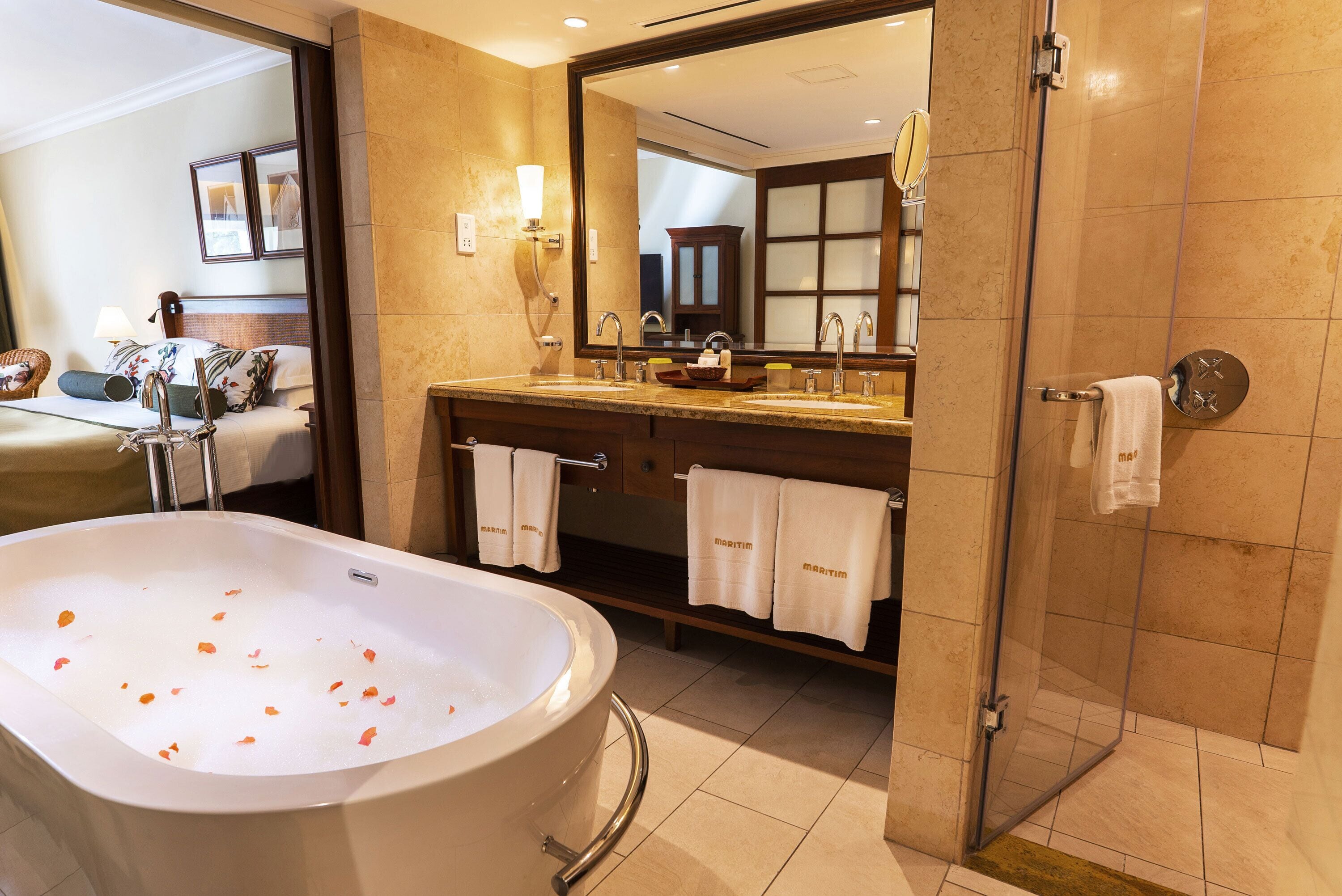 A hotel bathroom with a large bathtub, two sinks, a shower, and a mirror.