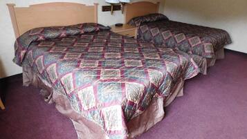 A room with two beds, each with a patterned quilt, a nightstand with a lamp, and a purple carpet.