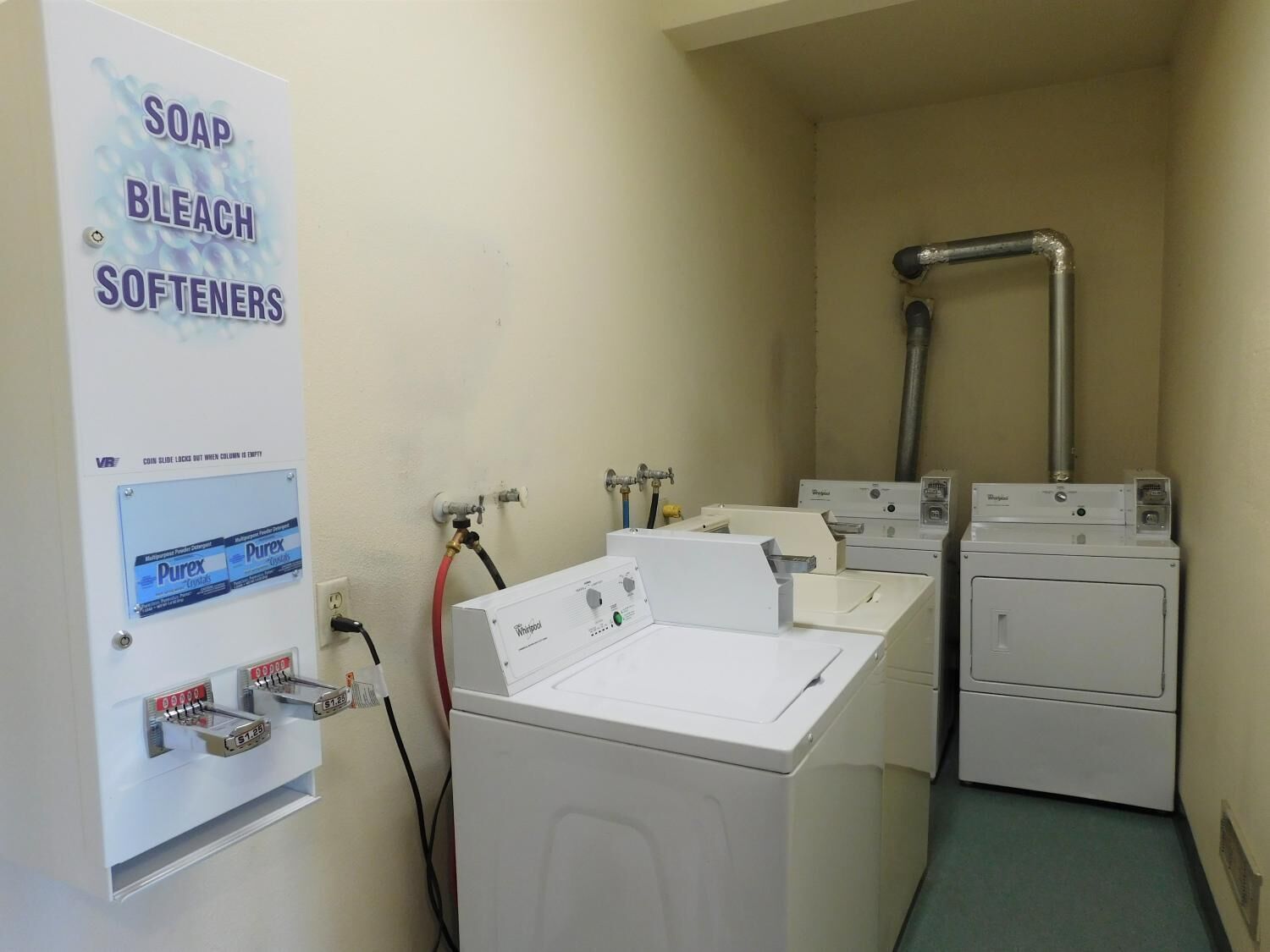 A laundry room with a sign for soap, bleach, and softeners. There are two washing machines and a dryer.