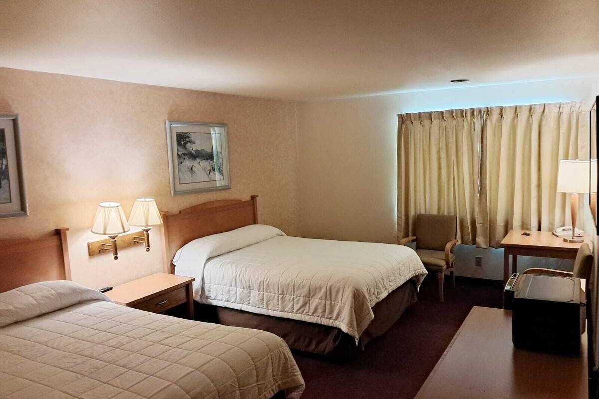 A hotel room with two beds, a desk, a chair, and a window with curtains.