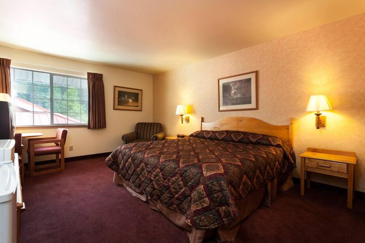 A hotel room with a large bed, two bedside lamps, a chair, a small table, and a window with curtains.