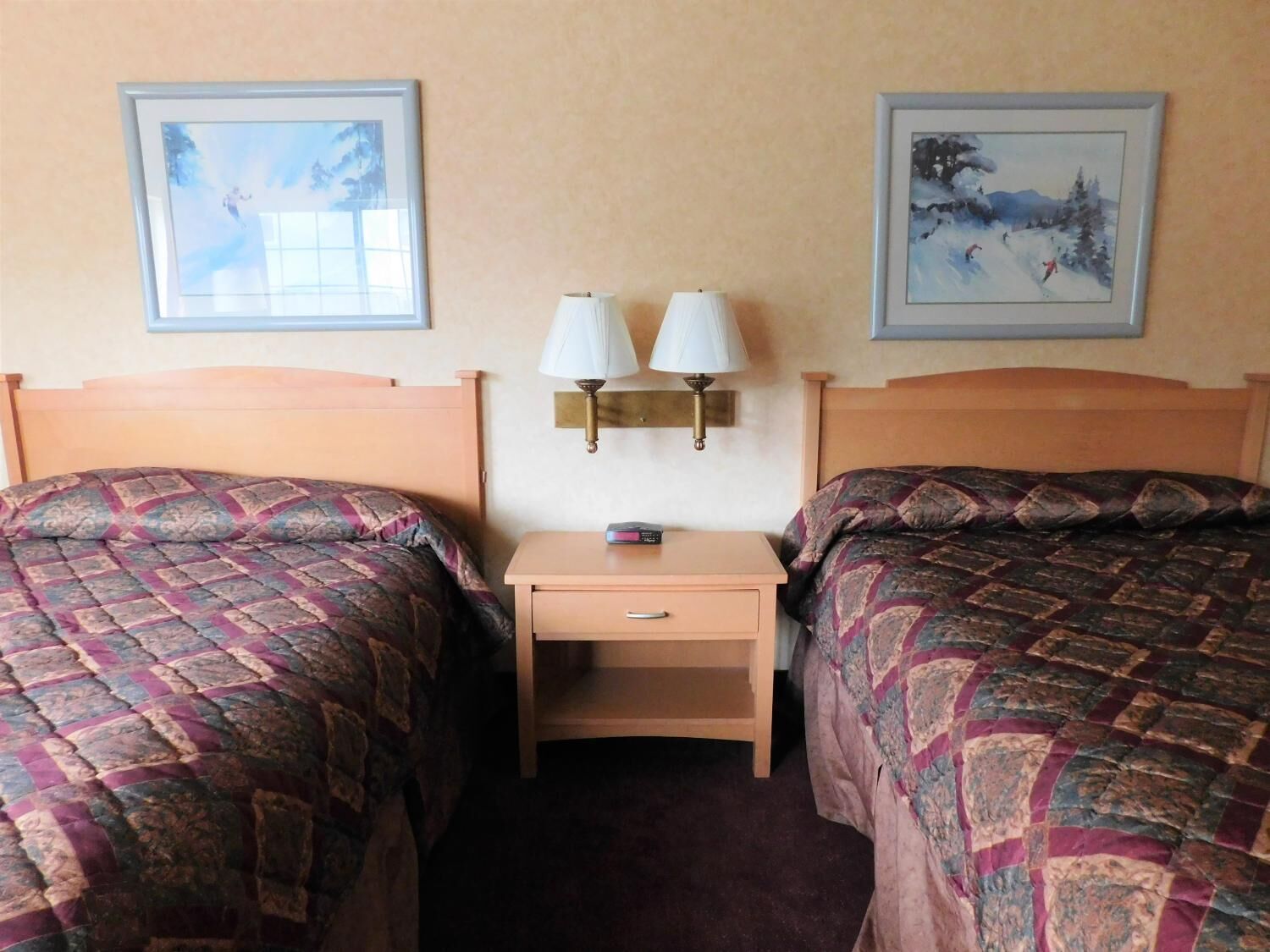 A hotel room with two beds, a nightstand, and two wall-mounted lamps.