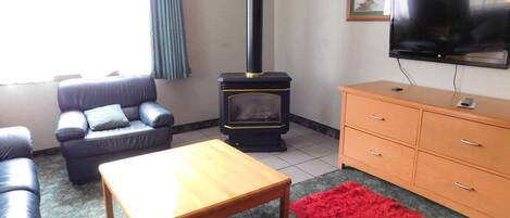 Ein Wohnzimmer mit einer Couch, einem Holztisch, einem roten Teppich, einem Fernseher und einem Kamin.