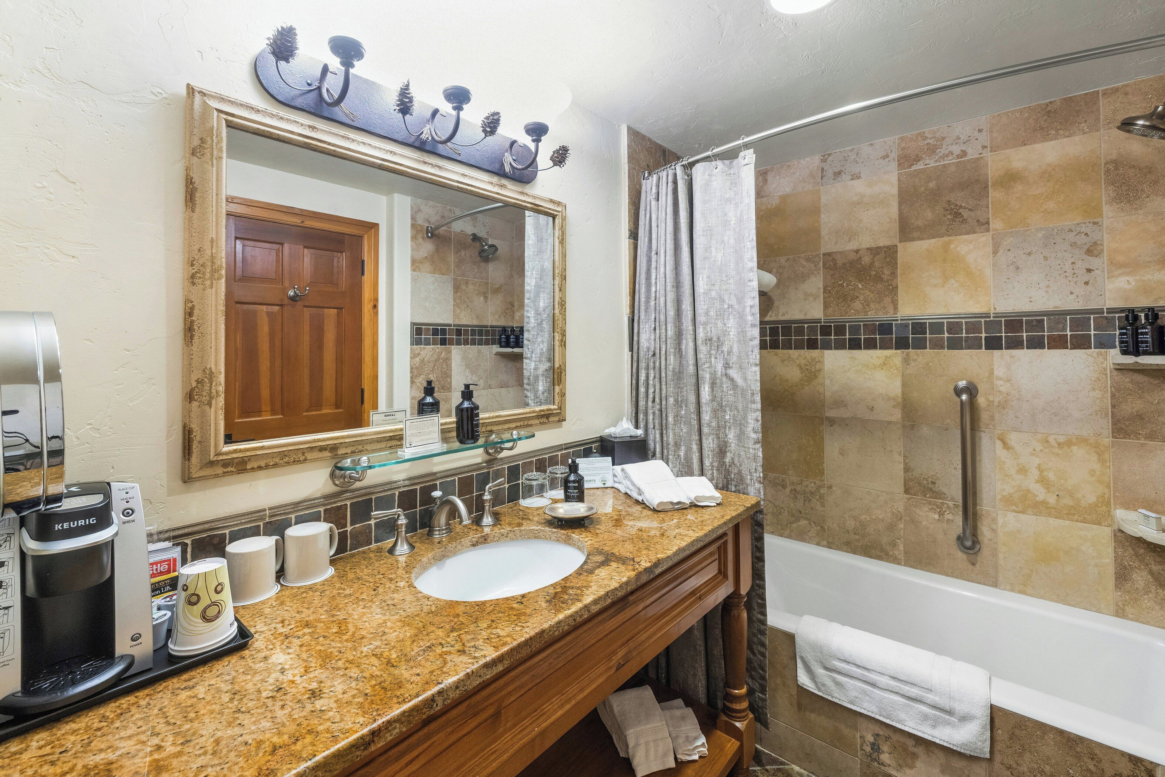 A bathroom with a sink, mirror, coffee maker, and shower.