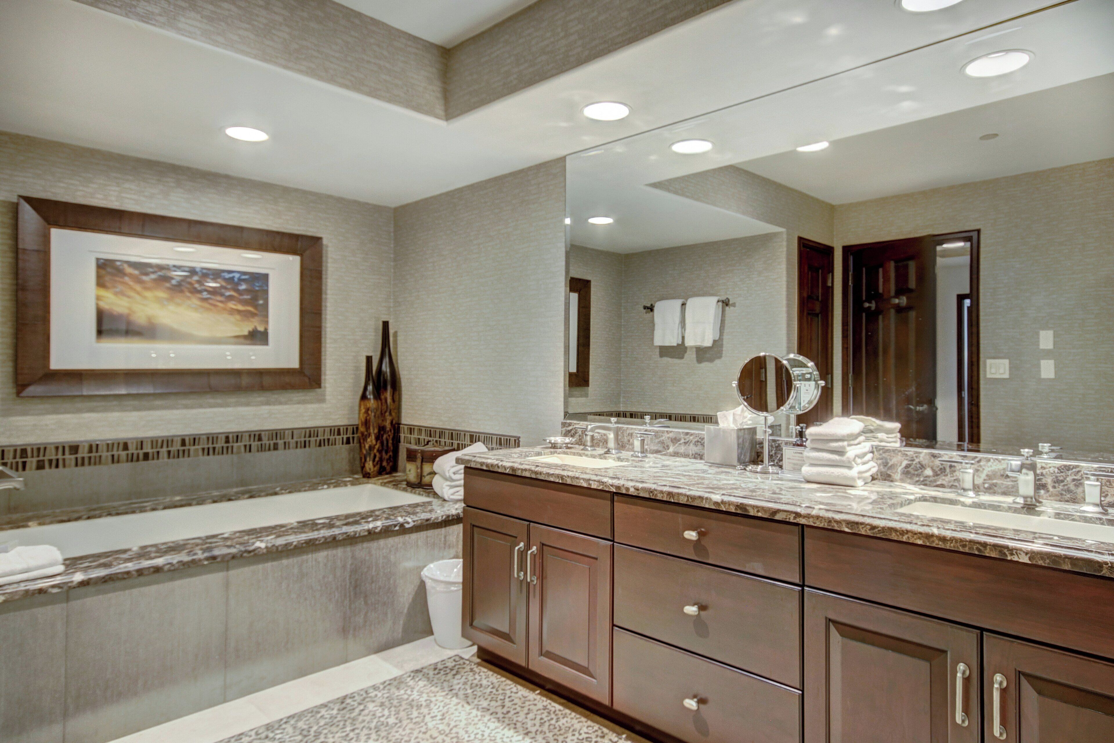 A modern bathroom with a large mirror, a bathtub, and a vanity with a sink.