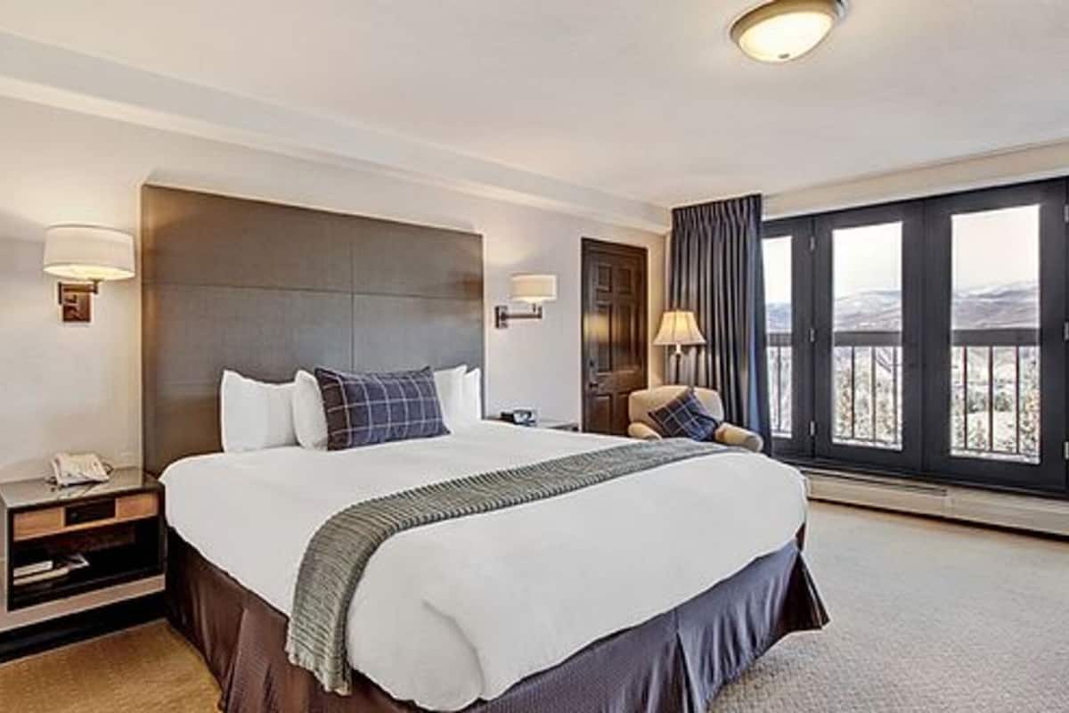 Habitación de hotel con una cama grande, mesitas de noche, una silla y vistas al exterior.
