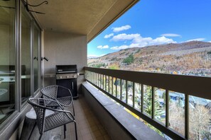 Un balcón con una parrilla, sillas y vistas a un paisaje montañoso.