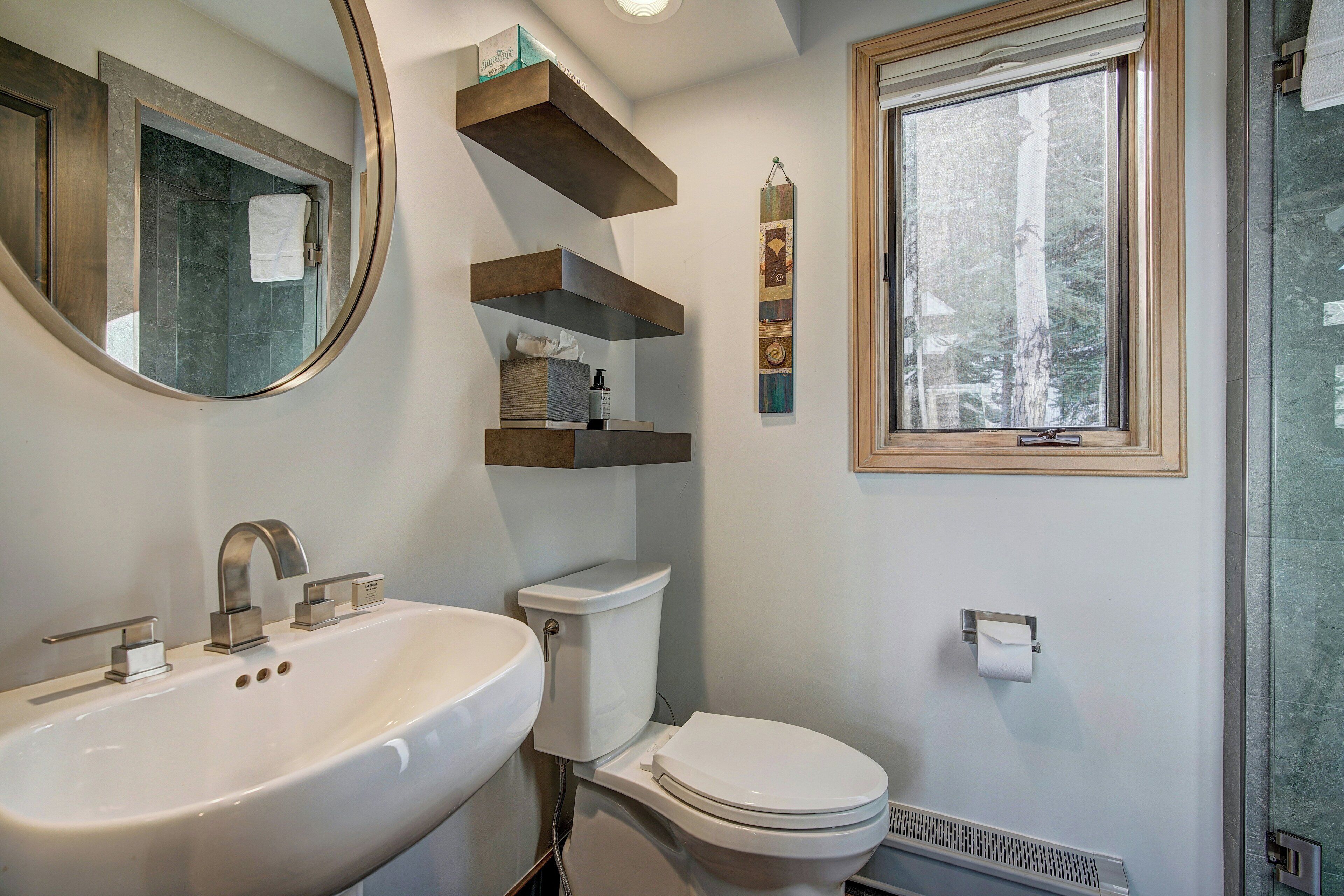 Une salle de bain avec un lavabo, des toilettes et une fenêtre. Des étagères sont fixées au mur au-dessus des toilettes.