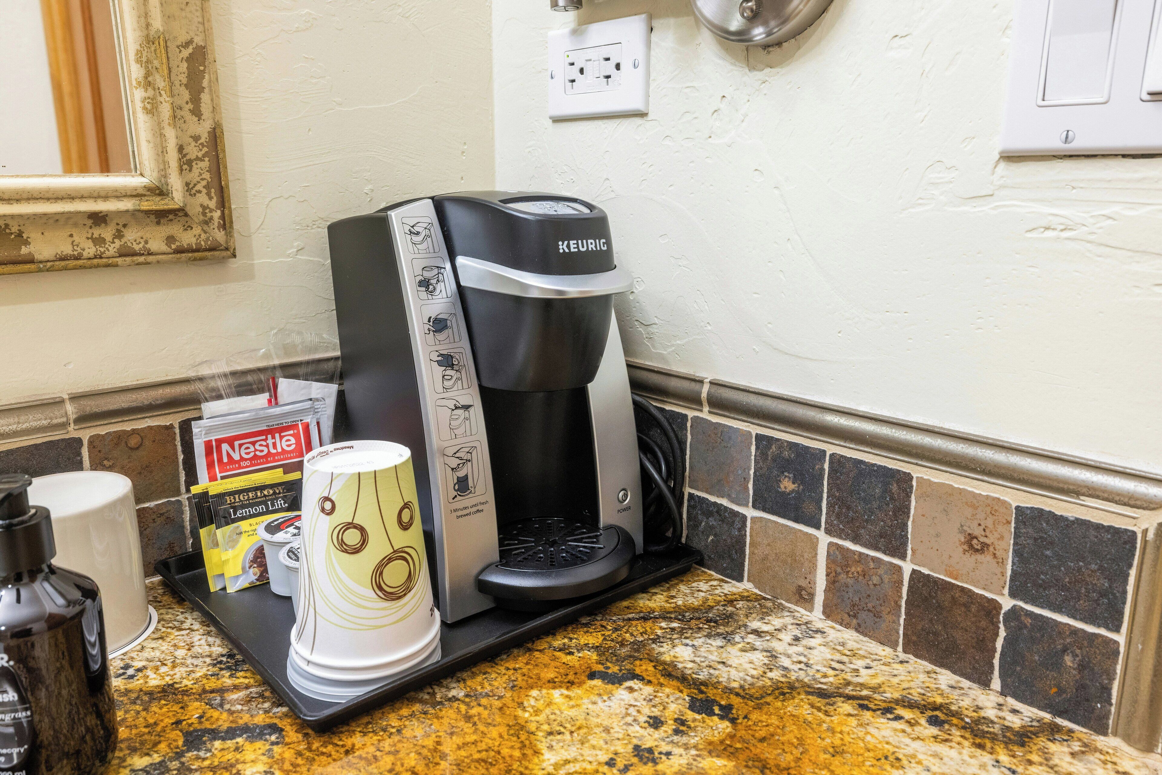 A coffee maker on a kitchen counter with a tray of disposable cups, a Nestle coffee pod, and a bottle of water.