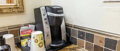 A coffee maker on a kitchen counter with a tray of disposable cups, a Nestle coffee pod, and a bottle of water.