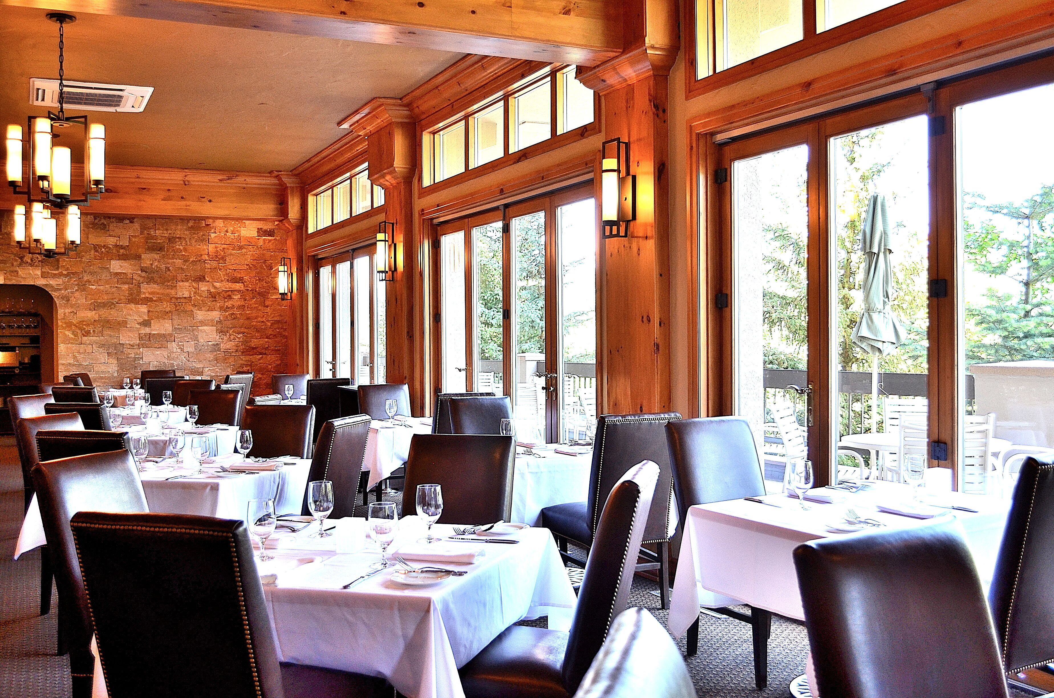 Un restaurante con varias mesas dispuestas para comer, ventanas amplias y una pared de piedra.