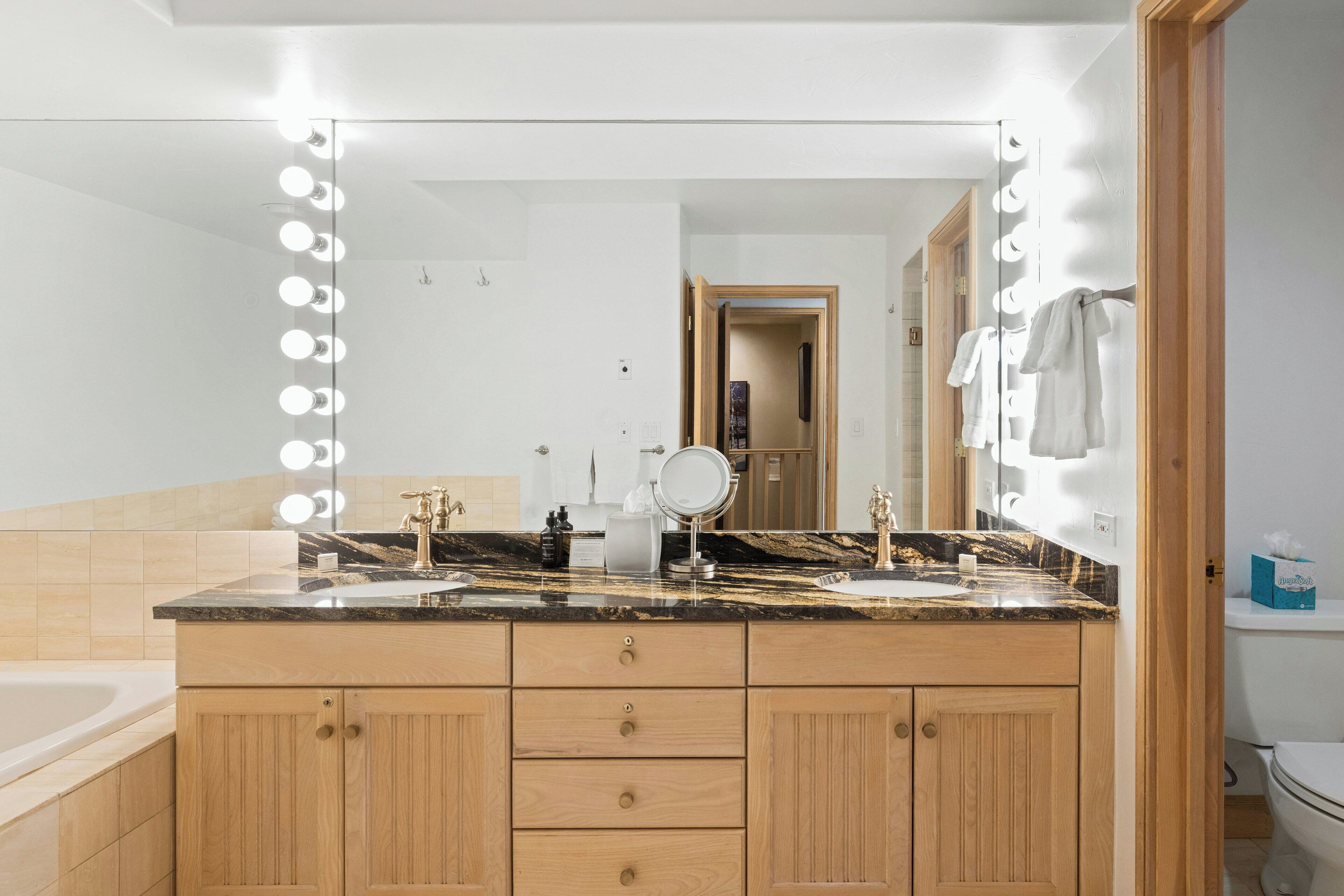 A bathroom with a vanity, a mirror with lights, a bathtub, and a toilet.
