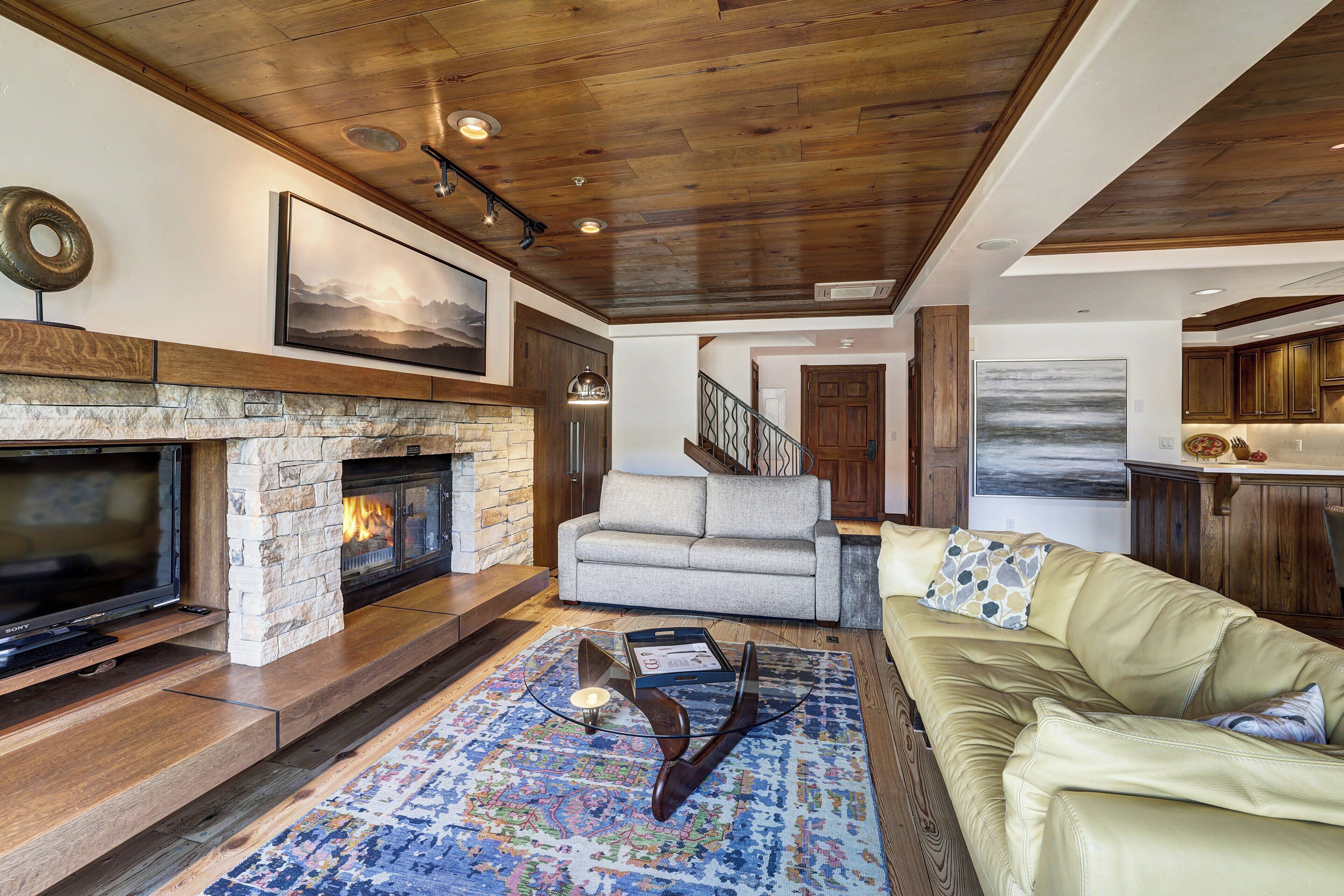 A living room with a stone fireplace, leather sofa, and a large rug.