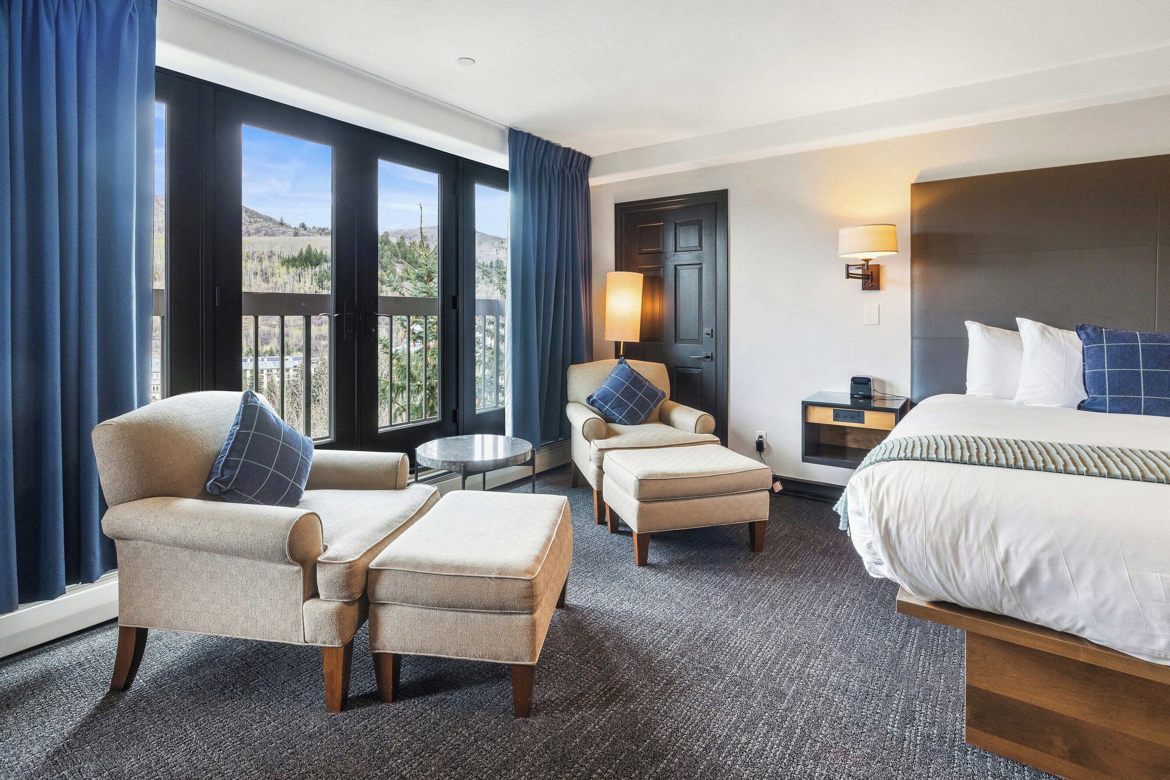 A hotel room with a large bed, two armchairs, a sofa, a small table, and a view of the outdoors.