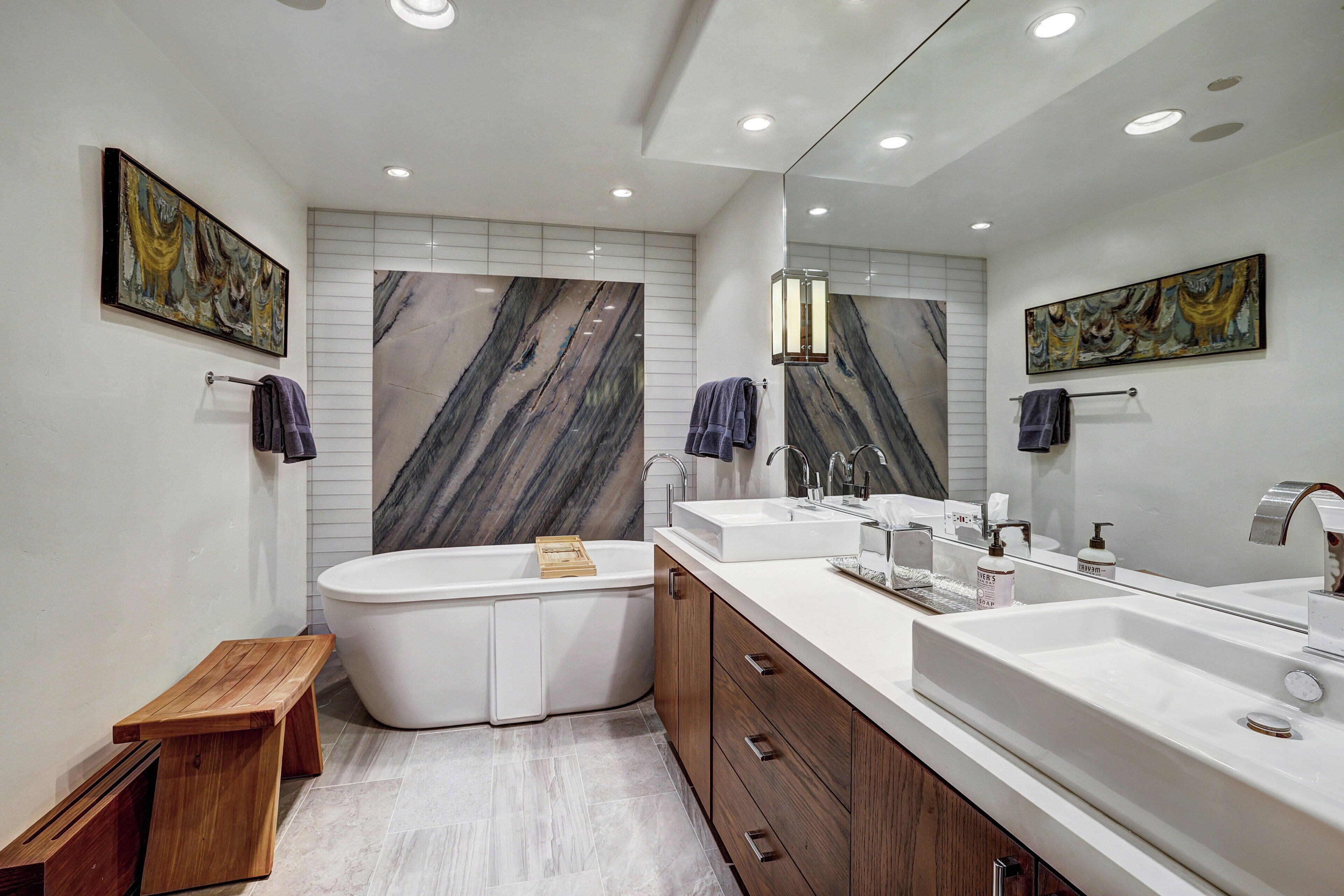 Un baño moderno con una bañera independiente, un tocador con un espejo grande y paredes con diseño de mármol.