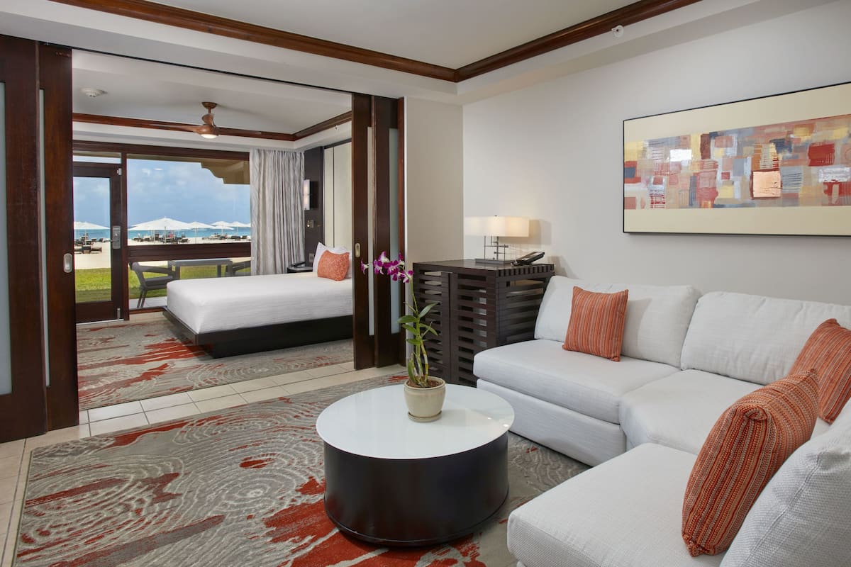 A hotel room with a bed, a sofa, a coffee table, a painting, and a view of the beach.