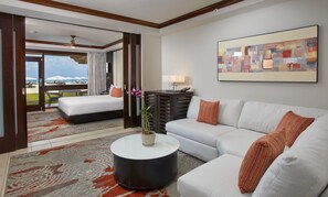 A hotel room with a bed, a sofa, a coffee table, a painting, and a view of the beach.