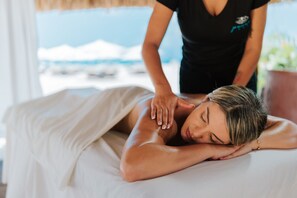 A person receiving a massage in a room with a view of the beach.
