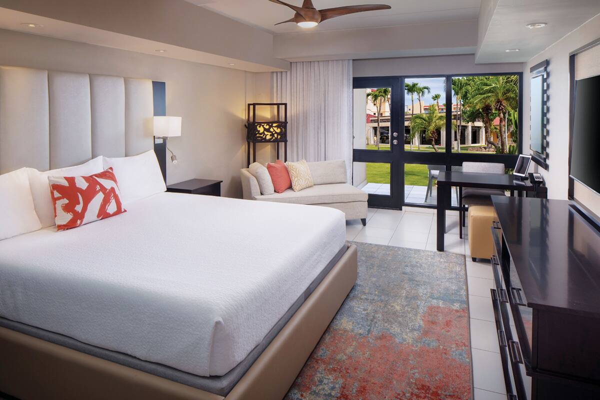 A modern hotel room with a large bed, a desk, and a view of the outdoors.