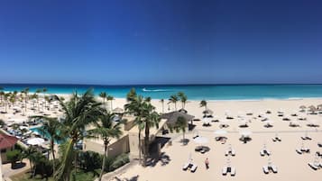 A beach resort with multiple sun loungers and umbrellas, a pool, and palm trees.
