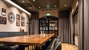Una sala conferenze con un lungo tavolo in legno, sedie grigie e quadri appesi al muro.