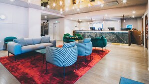 Una hall moderna con una reception, area salotto con poltrone a fantasia e tappeto rosso.