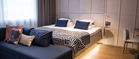 Una habitación de hotel moderna con sofá, dos camas, una mesita de noche y una silla.