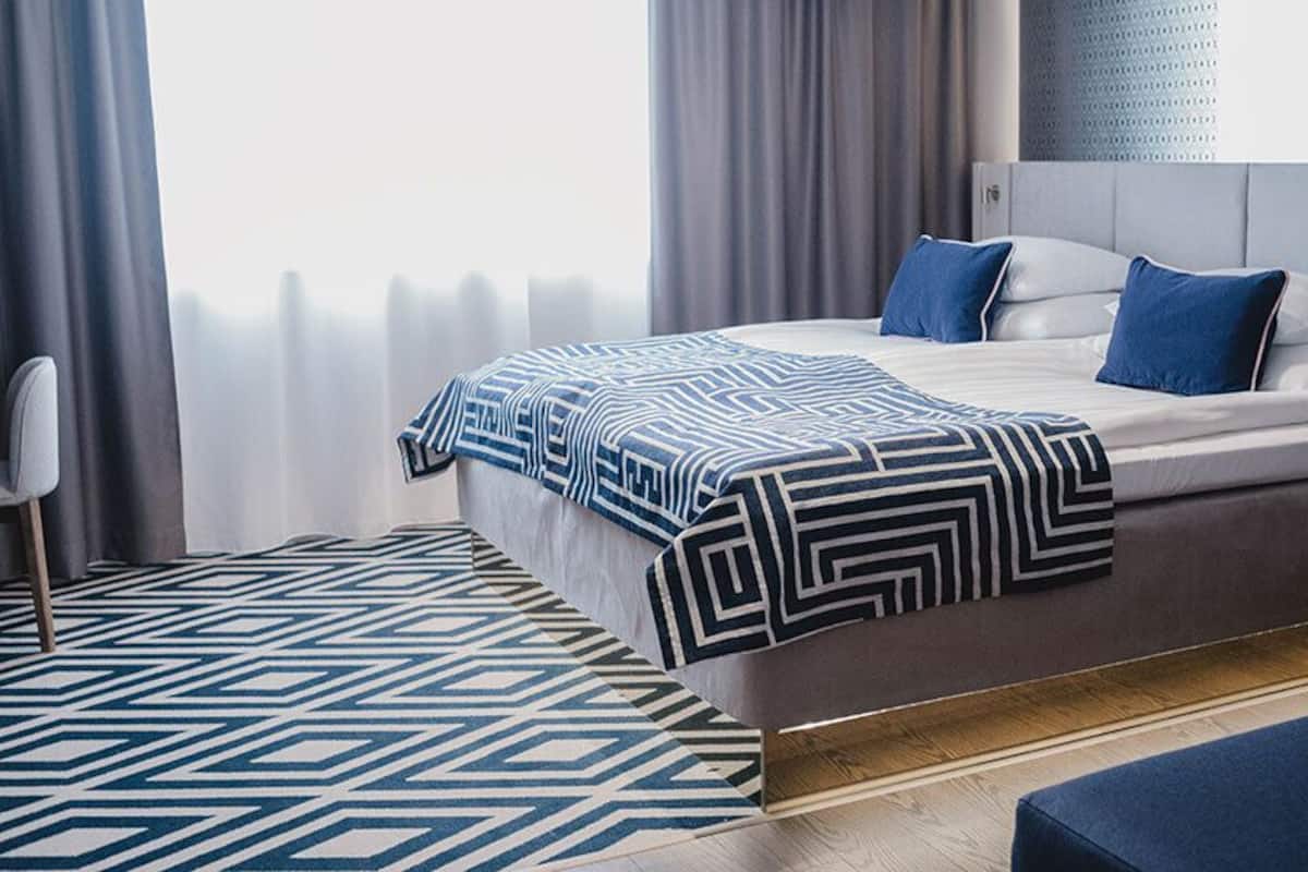 A modern hotel room with a bed, a chair, and a patterned rug.