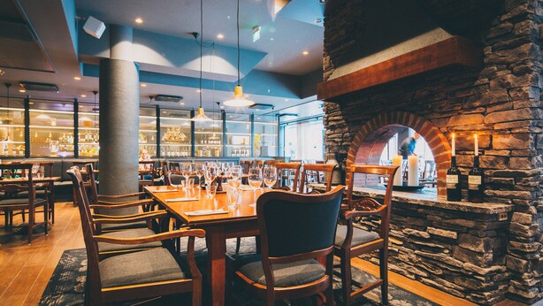 Un interno ristorante con tavoli e sedie in legno, pareti in pietra e lampade pendenti.